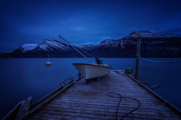 Boat docked at pier with mountains at night