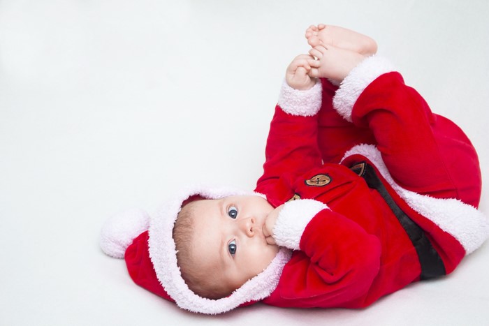 Baby in Santa Claus costume lying on white background