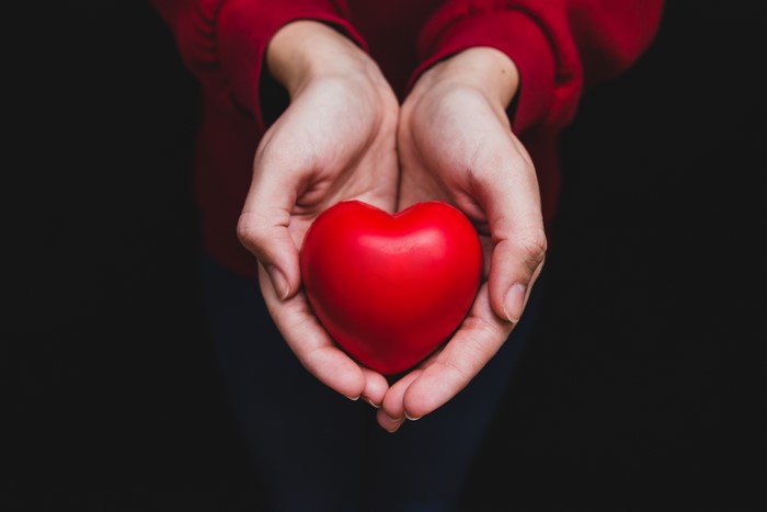 Hands holding a red heart on a black background