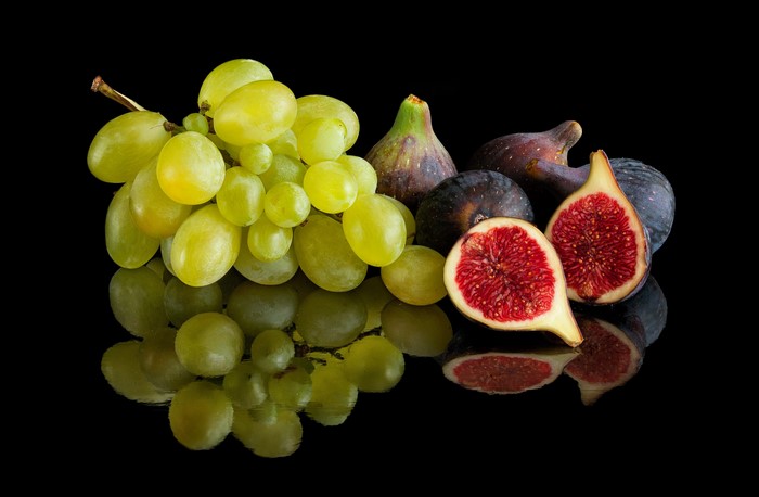 Green grapes and figs on a black background with reflection