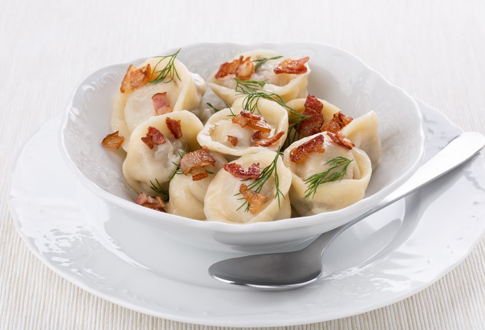 Pelmeni with bacon and dill on a plate with a spoon