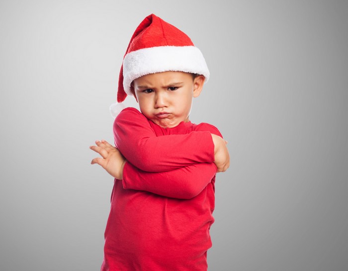 Boy in Santa hat frowning with arms crossed