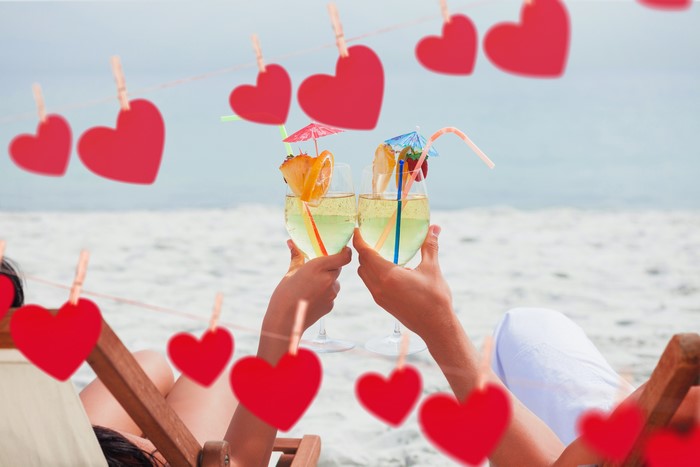 Couple toasting with cocktails on beach with hearts