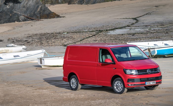 Red Volkswagen Transporter van on a beach with boats
