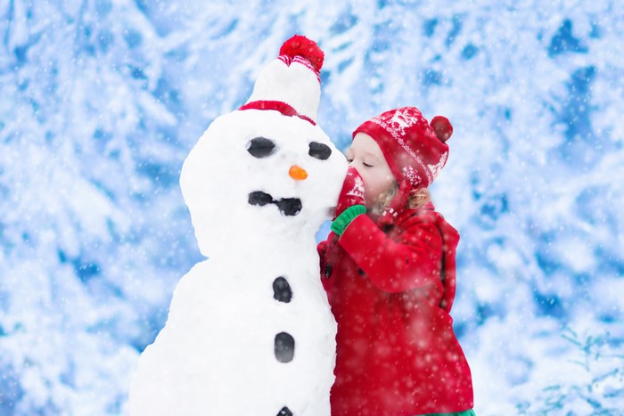 Little girl in red hat and coat building a snowman