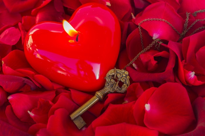 Red heart candle and key on rose petals