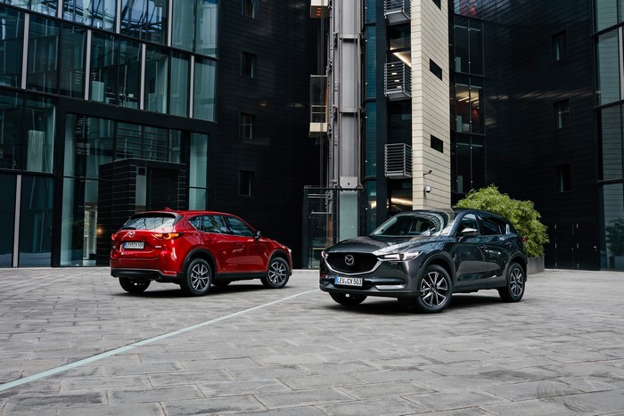 Two Mazda CX-5 cars in front of modern buildings