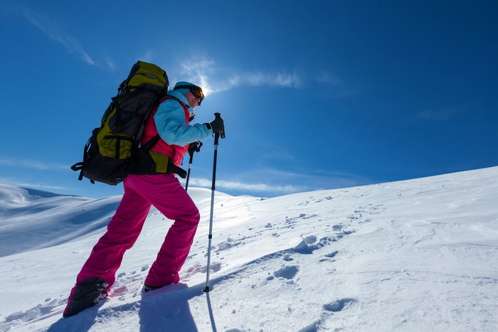 Woman hiking up a snowy mountain with ski poles