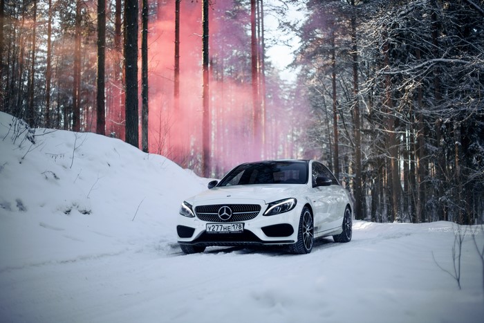 White Mercedes-Benz C450 in snowy forest with pink smoke