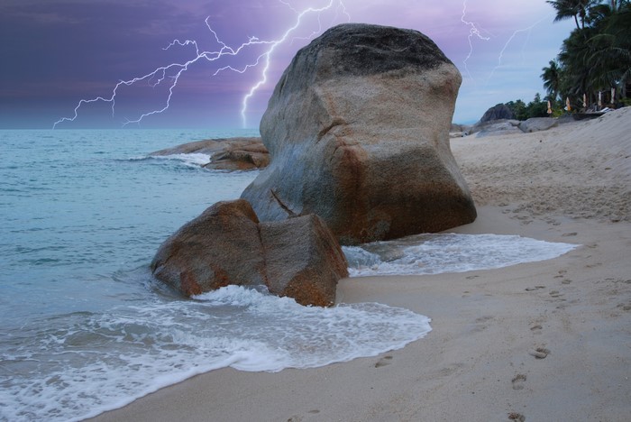 Lightning strikes over a beach with large boulders in Thailand