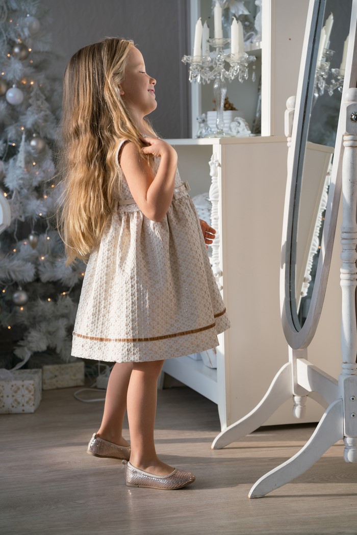 Girl in a dress looking in a mirror near a Christmas tree