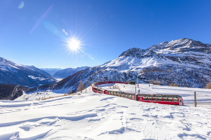 Red train in snowy Swiss Alps with sun