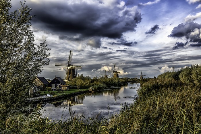 Windmills and river in Kinderdijk, Netherlands under cloudy sky