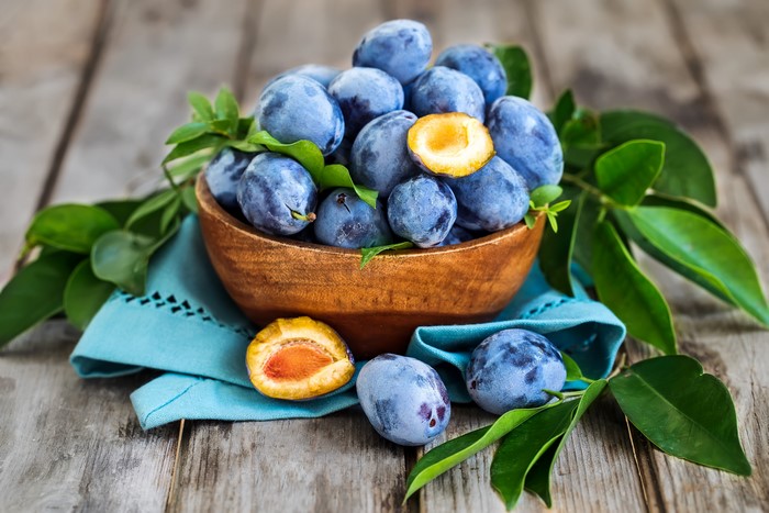 Plums in a wooden bowl with leaves