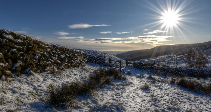 Snowy landscape with stone wall and sun in England