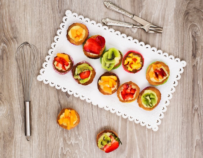 Fruit tarts on a white doily with a whisk