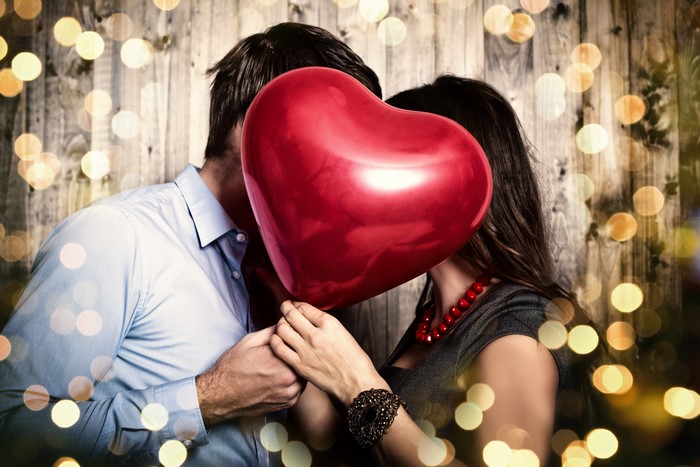 Couple kissing behind a red heart balloon