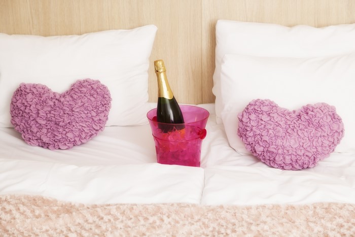 Champagne bottle between heart pillows on a bed