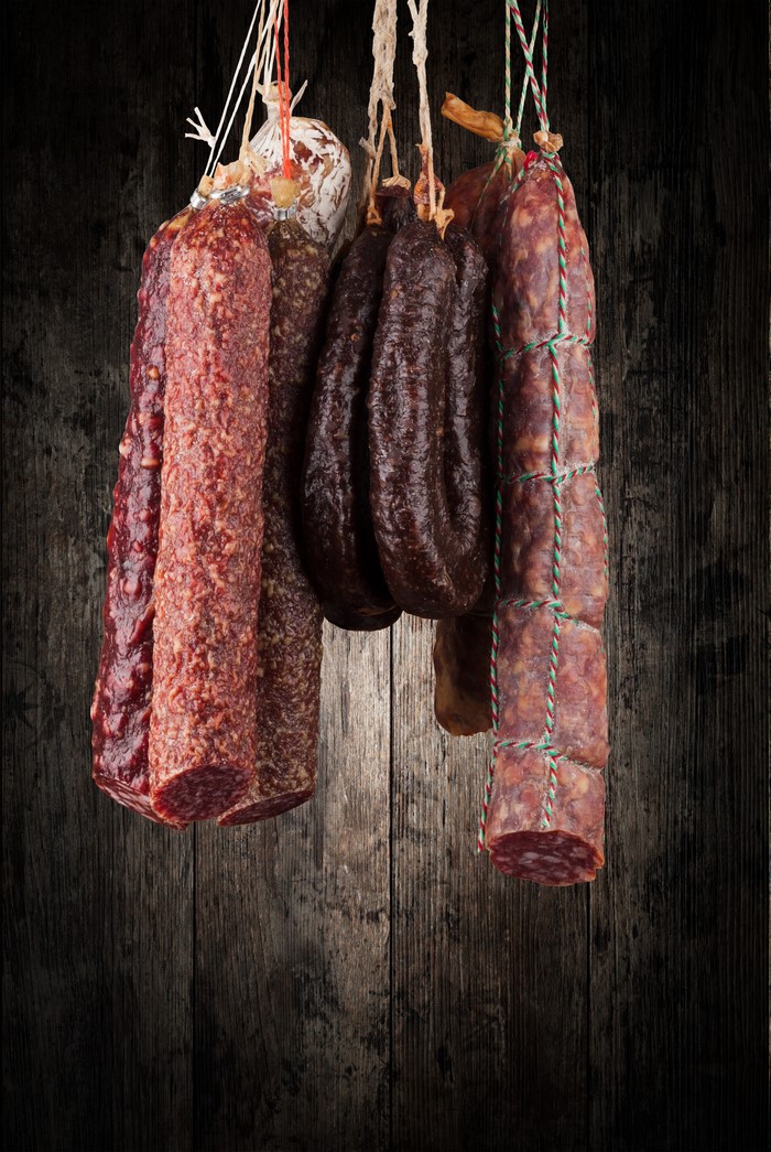 Various sausages hanging on a wooden background