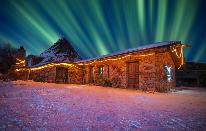 Stone house with aurora borealis and fairy lights in winter