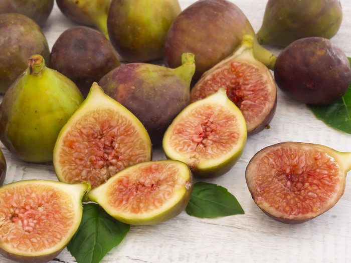 Common figs, some whole and some halved, on a white wooden surface