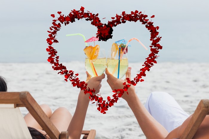 Couple toasting cocktails on beach with heart overlay