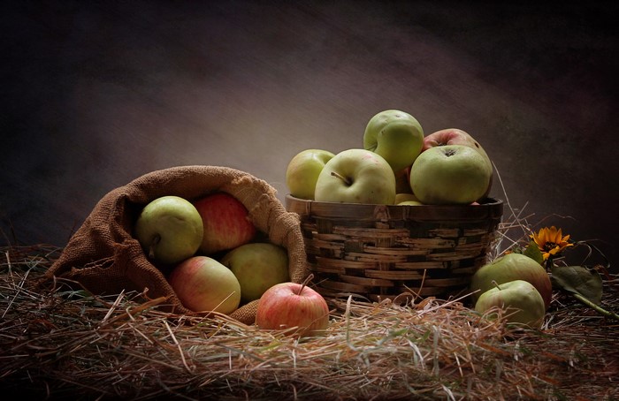 Apples in a burlap sack and wicker basket on straw