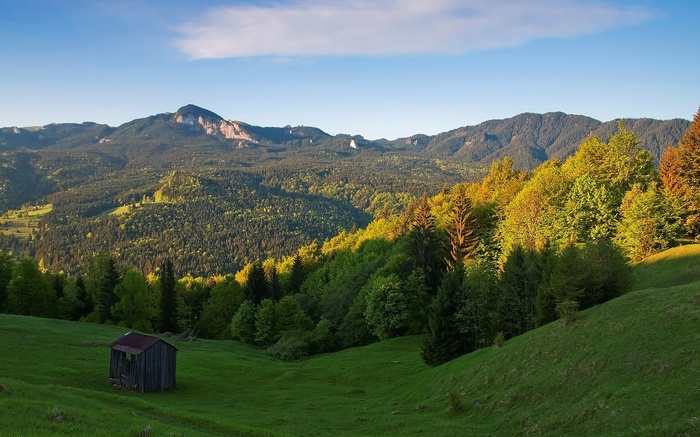 Wooden shed on a grassy hill with mountains in the background