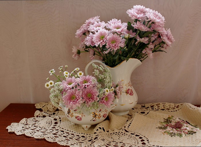 Pink chrysanthemums in decorative vases on a doily