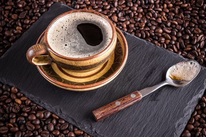 Coffee cup and spoon on slate with coffee beans