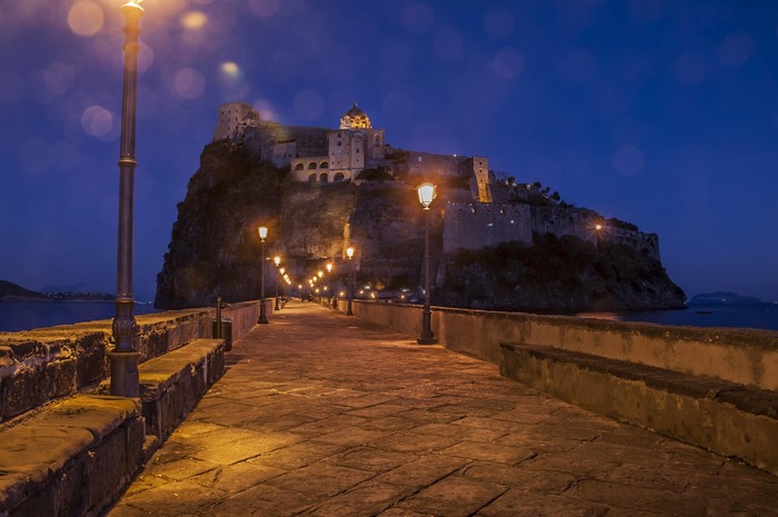 Aragonese Castle on a crag at dusk with street lights