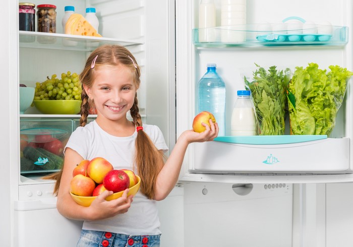 Girl holding apples in front of an open refrigerator