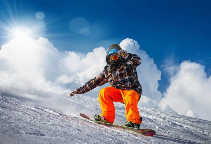 Man snowboarding down a snowy slope under a bright sun