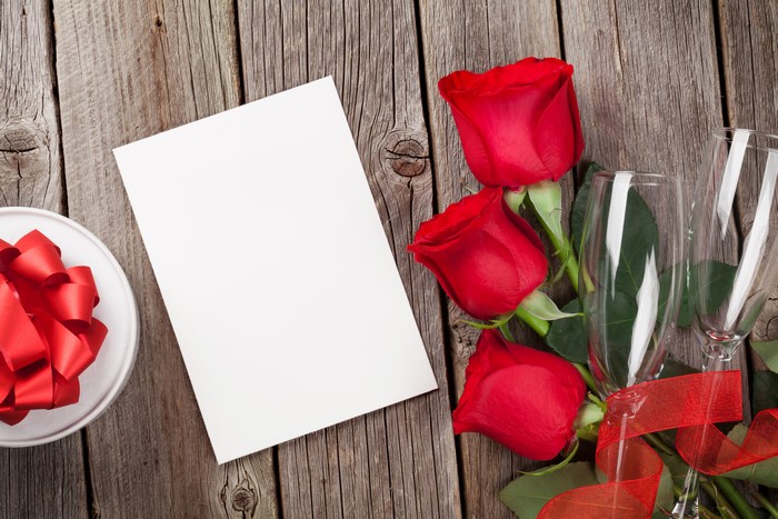 Red Roses, Champagne Glasses, Gift Box, and Card on Wood