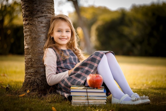 Girl sitting by a tree with books and an apple