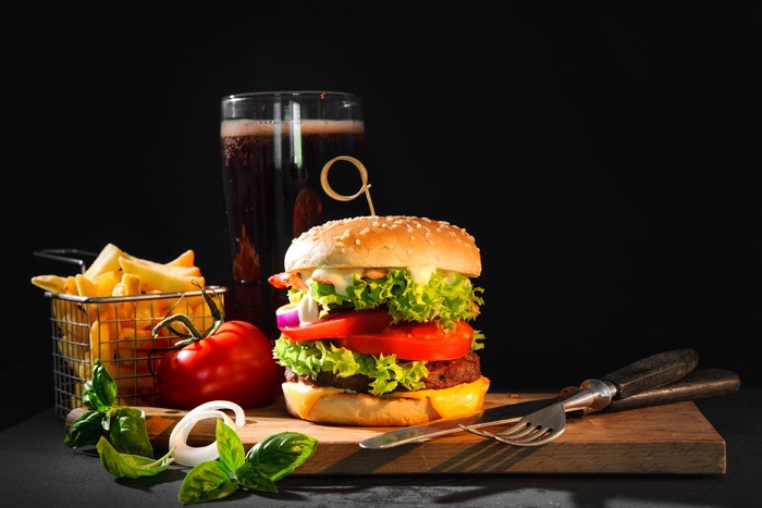 Hamburger with fries and a drink on a cutting board