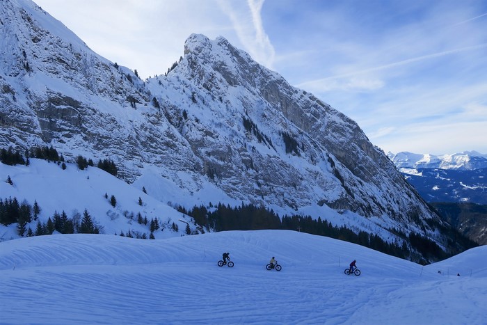 Three people fat biking on a snowy mountain slope in the Alps