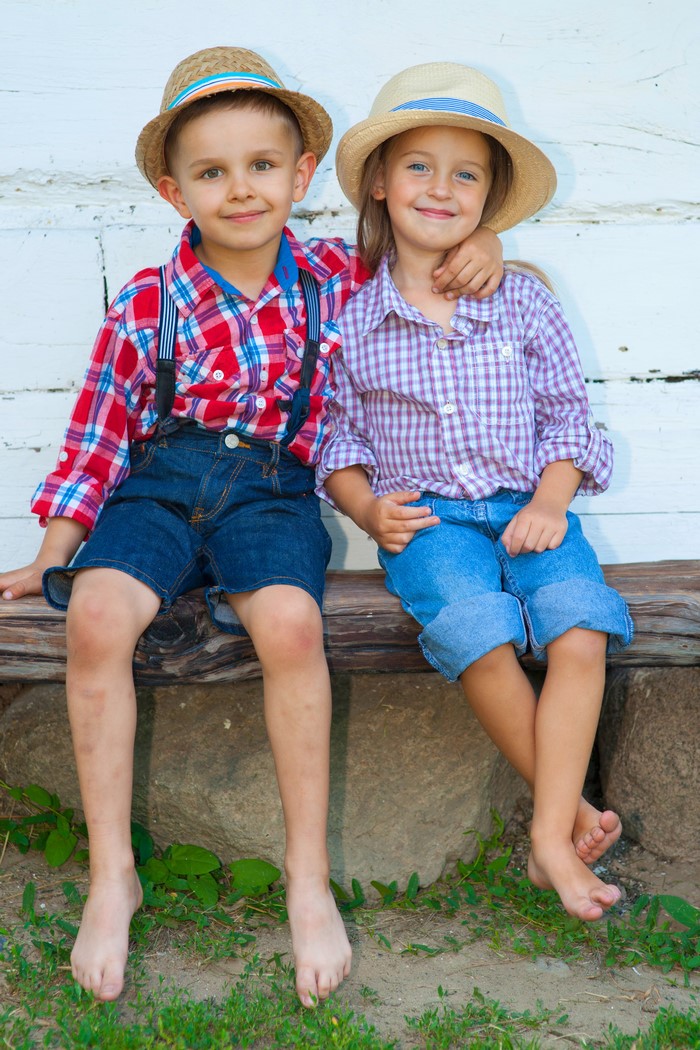 Two children wearing hats and plaid shirts sitting on a bench