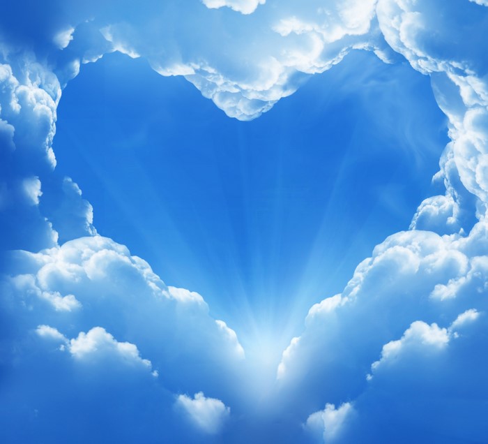 Heart shaped clouds in a blue sky with sun rays