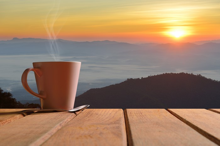 Coffee mug with steam at sunrise over mountains