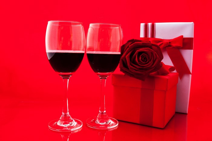 Two glasses of red wine with gifts and a rose