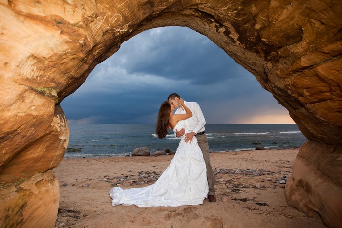 Bride and Groom kissing on a beach under a rock arch