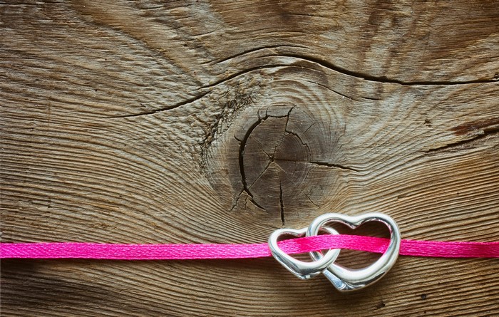 Two silver hearts intertwined with pink ribbon on wood