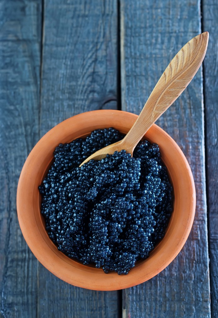 Black caviar in a clay bowl with a wooden spoon