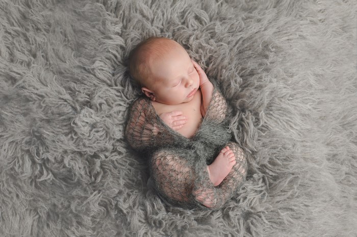 Newborn baby sleeping on a grey fluffy rug