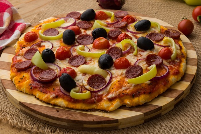 Pizza with pepperoni, olives, and vegetables on a cutting board
