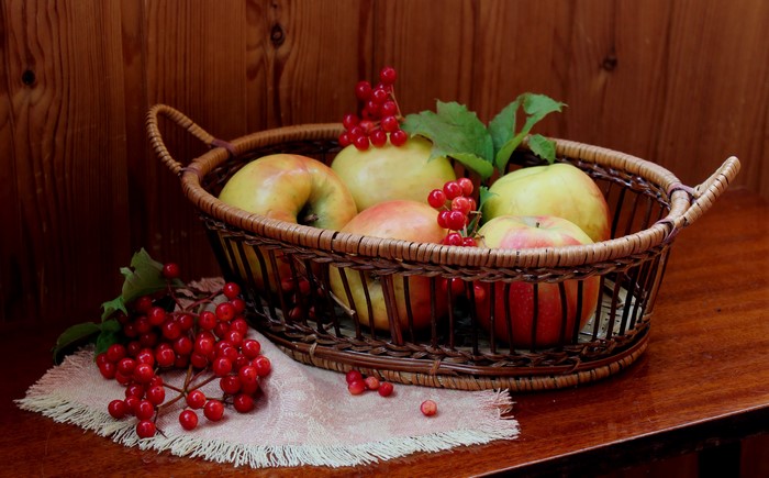 Apples and red berries in a wicker basket on a wooden table