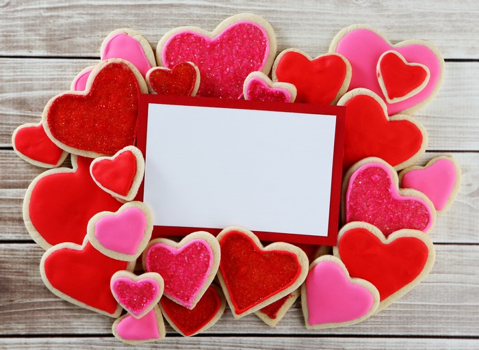 Heart-shaped cookies surrounding a blank card on wood