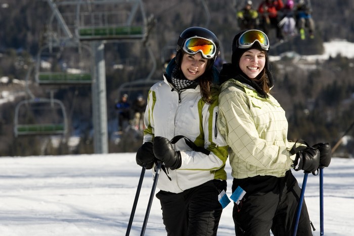 Two smiling women in ski gear on a snowy slope with ski lift