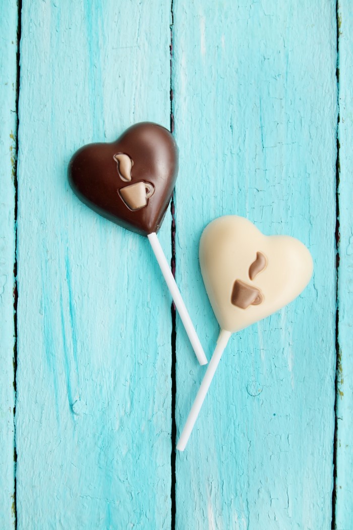 Two heart-shaped chocolate lollipops on blue wood